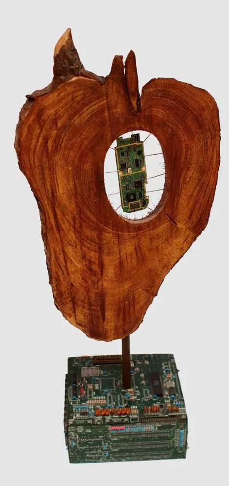 A dragon tree trunk shaped like a heart, mounted on a square base of computer motherboards. At the center of the heart is a mobile phone circuit board.